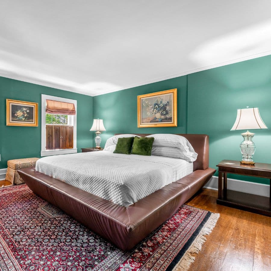 A cozy bedroom featuring a large bed, green walls, and decorative lamps.