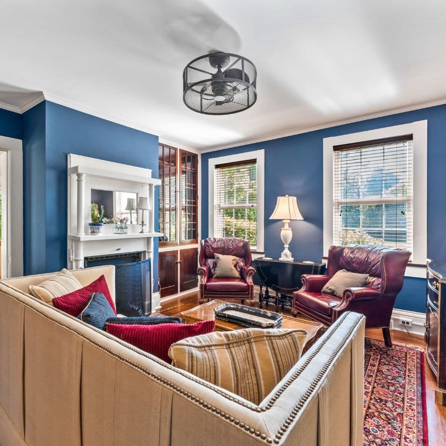 A cozy living room featuring a sofa with colorful cushions, two leather armchairs, and blue walls.
